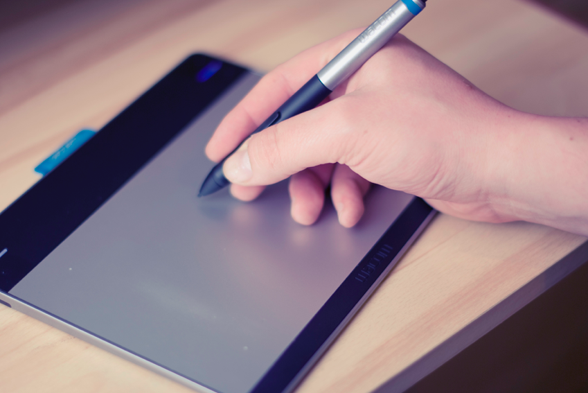 Stock photograph of a hand holding a stylus up to a drawing tablet