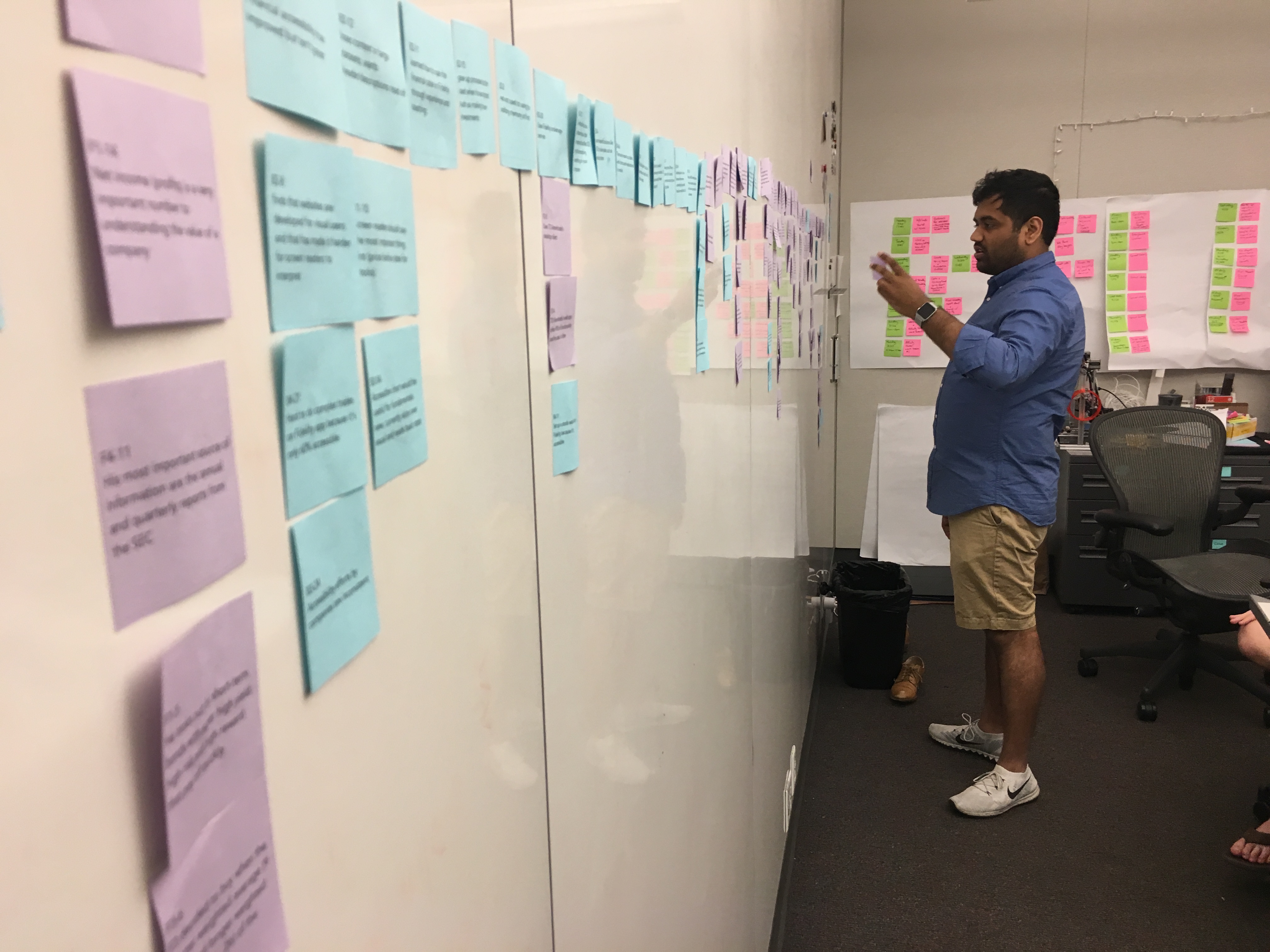 A male stands in front of a wall of blue and purple post-it notes with illegible printed text.