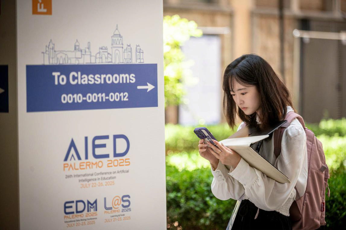 Cindy stands outside near signage for the 3 conferences while using her phone