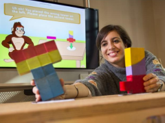 Nesra sits at a NoRILLA table and reaches for a tower of blocks