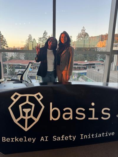 two master's students stand behind a basis sign during the hackathon