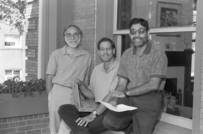 three researchers gather on the porch of a home while holding paper and a laptop
