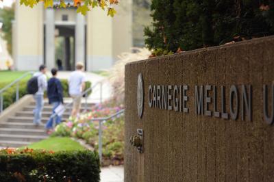 Carnegie Mellon University stone sign in the foreground, people walking up steps in the background