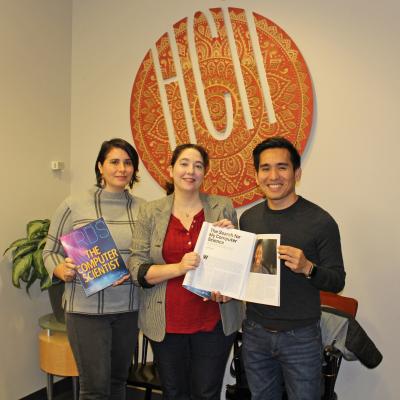 three PhD students hold paper copies of the Computer Scientist issue of the XRDS magazine, standing in the HCII lobby