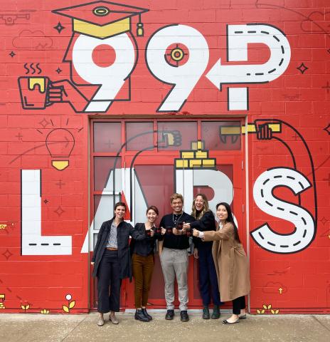 5 team members stand in front of a red wall with 99P Labs painted in white