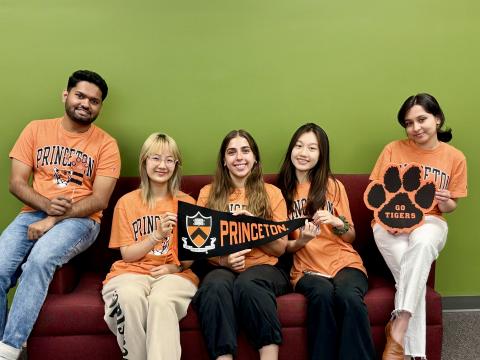 5 students wearing Princeton orange pose in front of The Green Wall