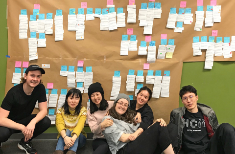 6 students on team Zazzle sit on the floor below their giant affinity diagram