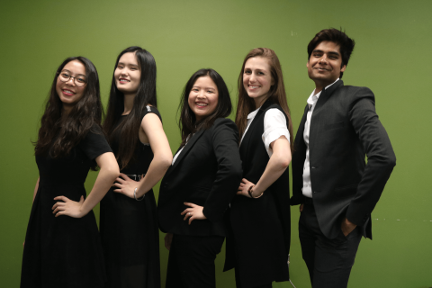 5 team members in black suits stand side by side in front of the MHCI green wall