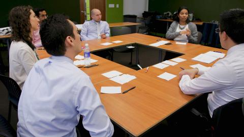 6 team members sit around 4 tables arranged in a square formation