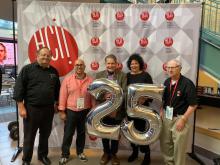 5 directors of the HCII stand in front of a banner and hold silver 25 balloons during the HCIIs 25th anniversary celebration