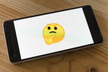 A mobile phone laying on a wooden table top. The screen is white with a yellow