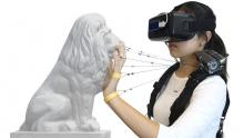 student wearing VR headset on face touches the face of a lion statue while wires connect fingers to the Wireality device on her shoulder
