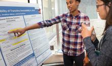 one SCS student points to her research poster and explains her work to another student 