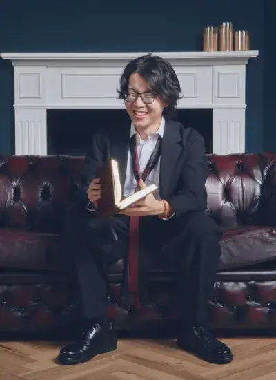 Photo of Riku Arakawa, HCII PhD Candidate, on leather couch in front of white fireplace