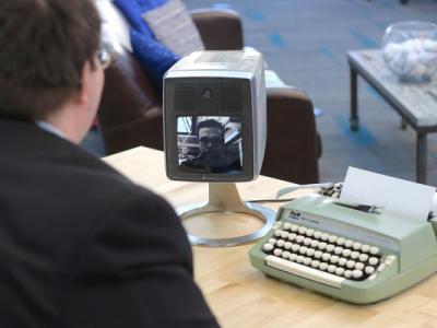over McGee's shoulder, picturephone and typewriter on table. Harrison speaks via picturephone