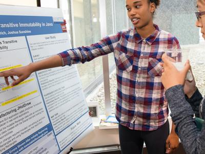 one SCS student points to her research poster and explains her work to another student 