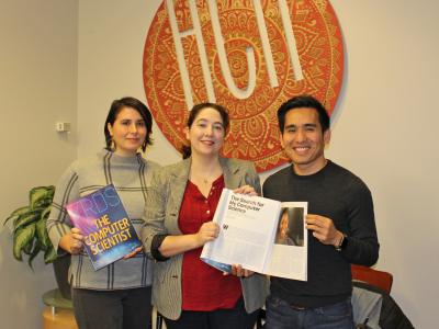 three PhD students hold paper copies of the Computer Scientist issue of the XRDS magazine, standing in the HCII lobby