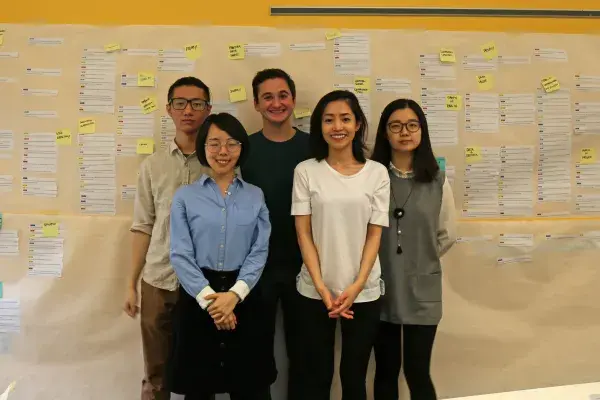 five METALS students stand by a large paper affinity diagram taped to a bright yellow wall