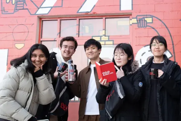 5 team members of the MHCI 99P labs team stands in front of a red wall painted with 99P