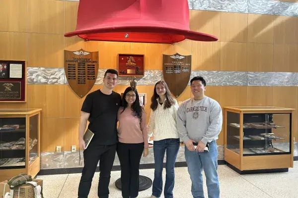Four team members of Team AirDrop stand under a large red hat