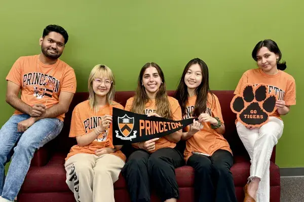 5 students wearing Princeton orange pose in front of The Green Wall