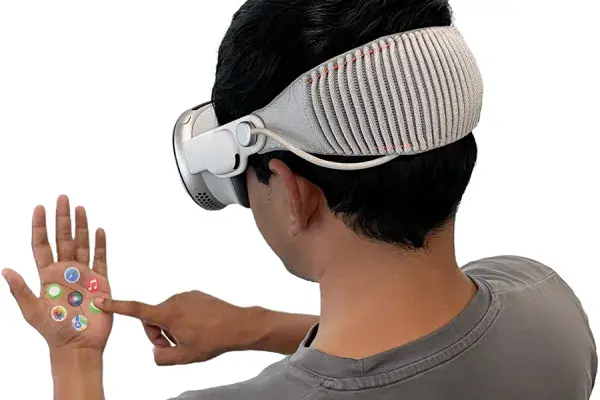 A man with dark hair wears a virtual reality headset and touches his palm, which is superimposed with icons for popular smartphone apps.