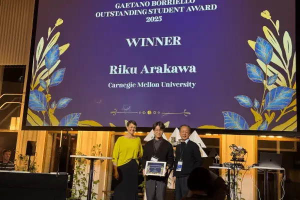 2 people from UbiComp present the Borriello Outstanding Student Award on stage to Arakawa