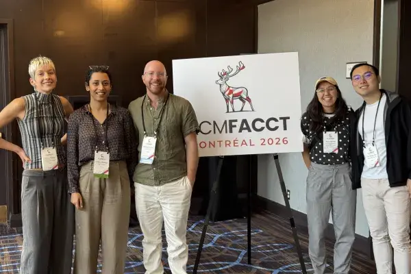 a small group of 5 community members stand near ACM FAccT signage 