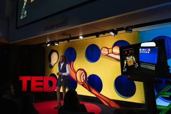Randi Williams stands on a stage beside large red TED letters, a screen nearby displays a robot 