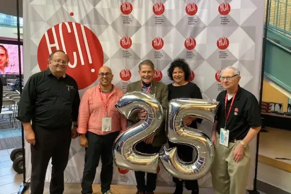 5 directors of the HCII stand in front of a banner and hold silver 25 balloons during the HCIIs 25th anniversary celebration