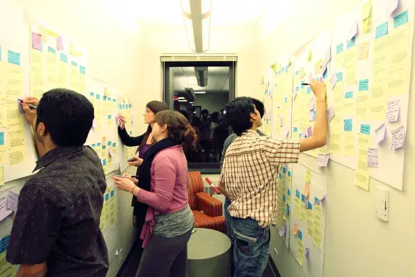 five students diagramming with colorful note paper on both walls of a narrow hallway 
