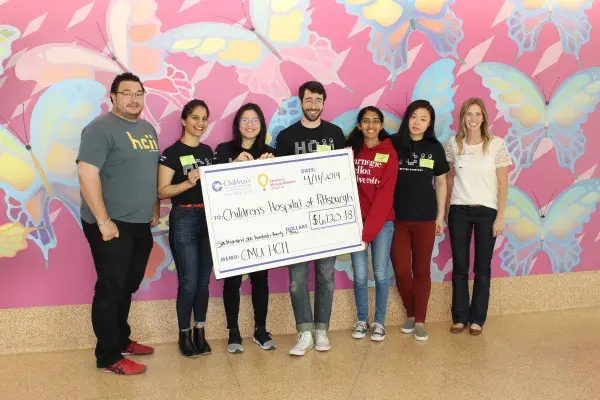 six people from CMU MHCI stand with rep from UPMC Foundation for check presentation at UPMC Children's Hospital