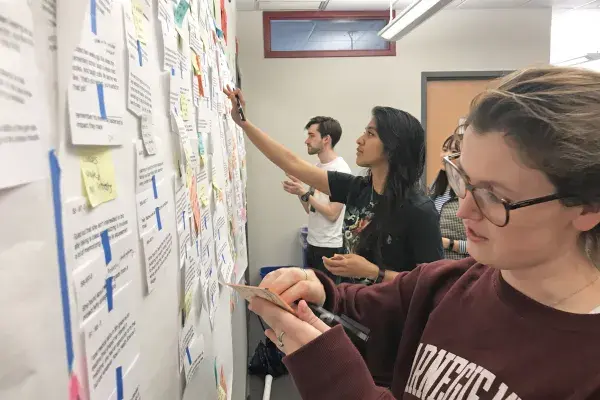 four MHCI students facing left side of photo, working on large affinity diagram on the wall