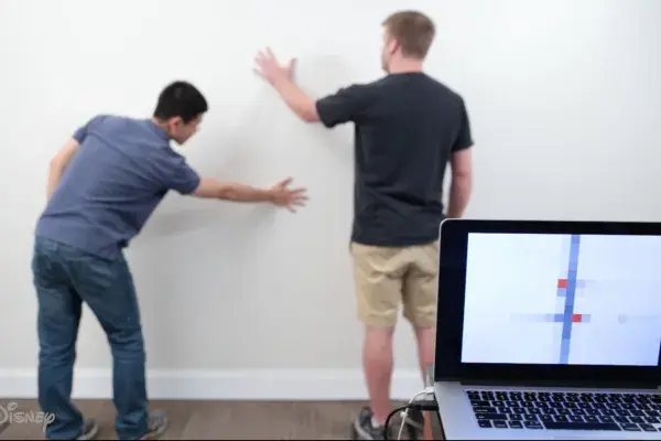 Wall++ technology developed by Carnegie Mellon University and Disney Research can turn an entire wall into a touchpad. It also serves a sensor for electromagnetic activity. Two men stand in front of a white wall. The locations of where they are touching the wall are visible on a nearby laptop screen.