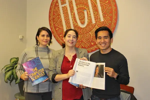 three PhD students hold paper copies of the Computer Scientist issue of the XRDS magazine, standing in the HCII lobby